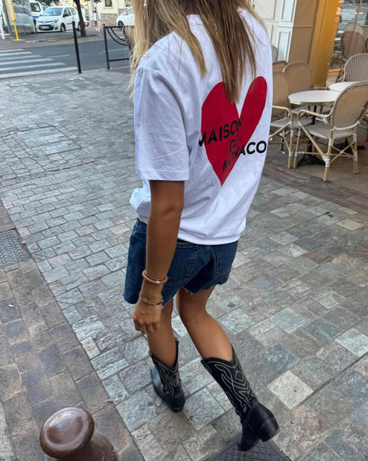 Person wearing a white t-shirt with a red heart design on a street.