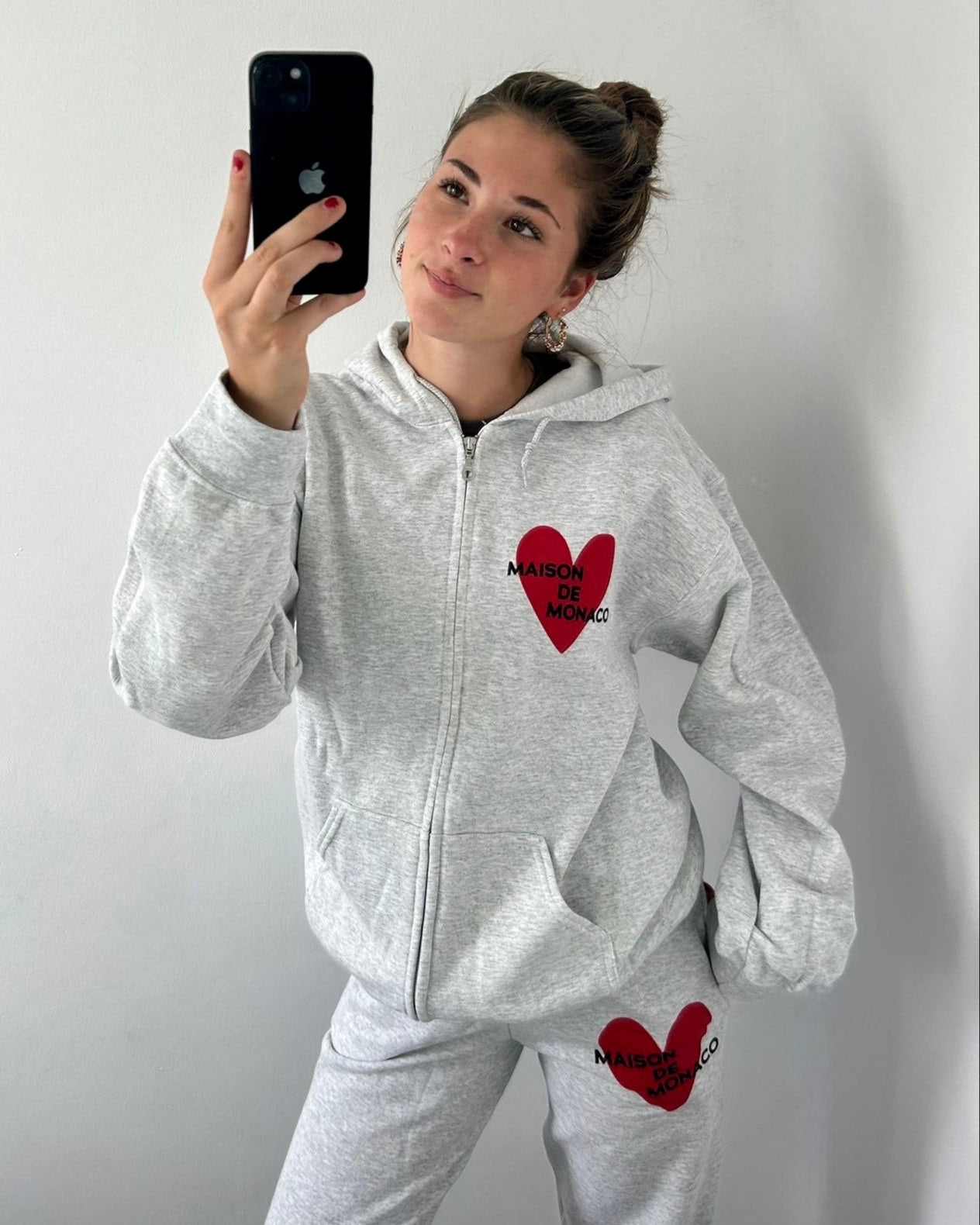 Person wearing a gray hoodie and pants with a red heart design, taking a mirror selfie.