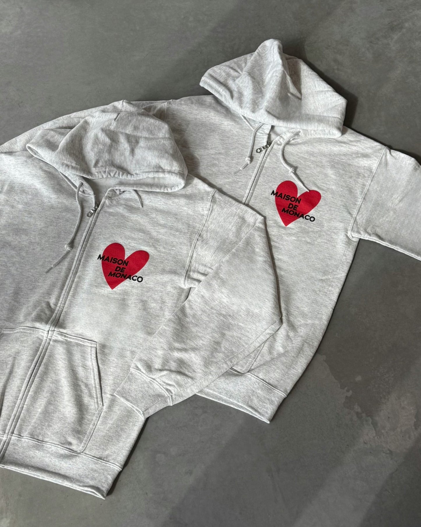 Grey zip-up hoodie with red heart designs on a gray surface